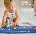 Toddler playing with the Winter Wonderland Advent Calendar, holding a wooden Christmas tree piece on a festive illustrated box.