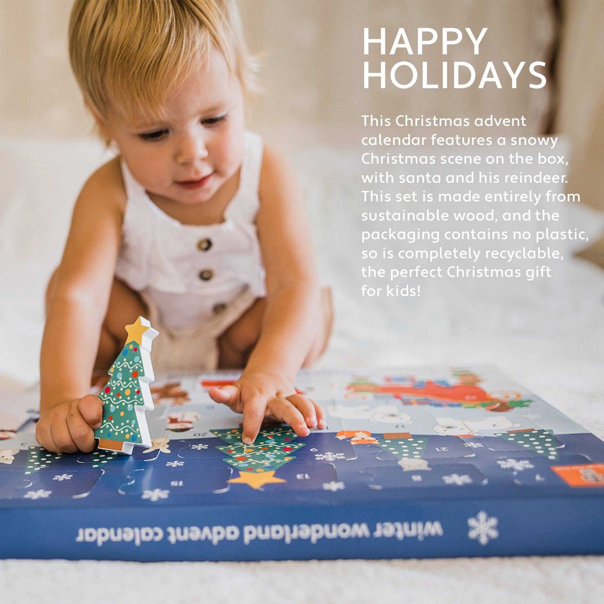 Toddler playing with the Winter Wonderland Advent Calendar, holding a wooden Christmas tree piece on a festive illustrated box.
