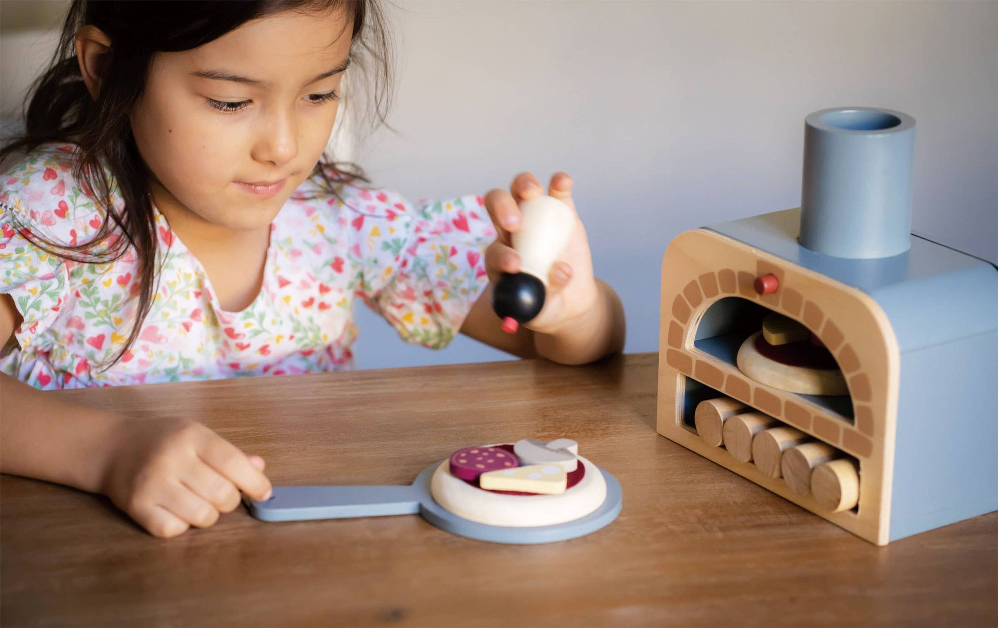 Child playing with Make Me a Pizza! - Wooden Pizza Oven Toy Play Set, assembling toppings and using the paddle for imaginative role play fun.
