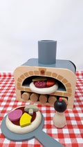 Make Me a Pizza! - Wooden Pizza Oven Toy Play Set displayed on red checkered cloth with pizza toppings and accessories for pretend play kitchens.