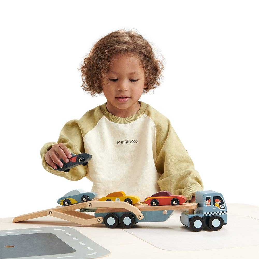 Toddler loading cars onto Tenderleaf Toys Wooden Car Transporter, promoting motor skills and creative play.